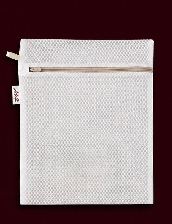 A white mesh zippered pouch with a small fabric tag on the left side, shown flat against a dark burgundy background.