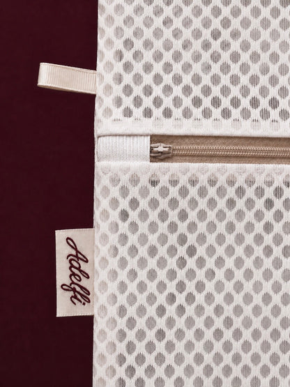 Close-up of a white mesh zippered pouch with a repeating geometric pattern, featuring a cream ribbon tab and a fabric tag with the brand name 'Accele'.